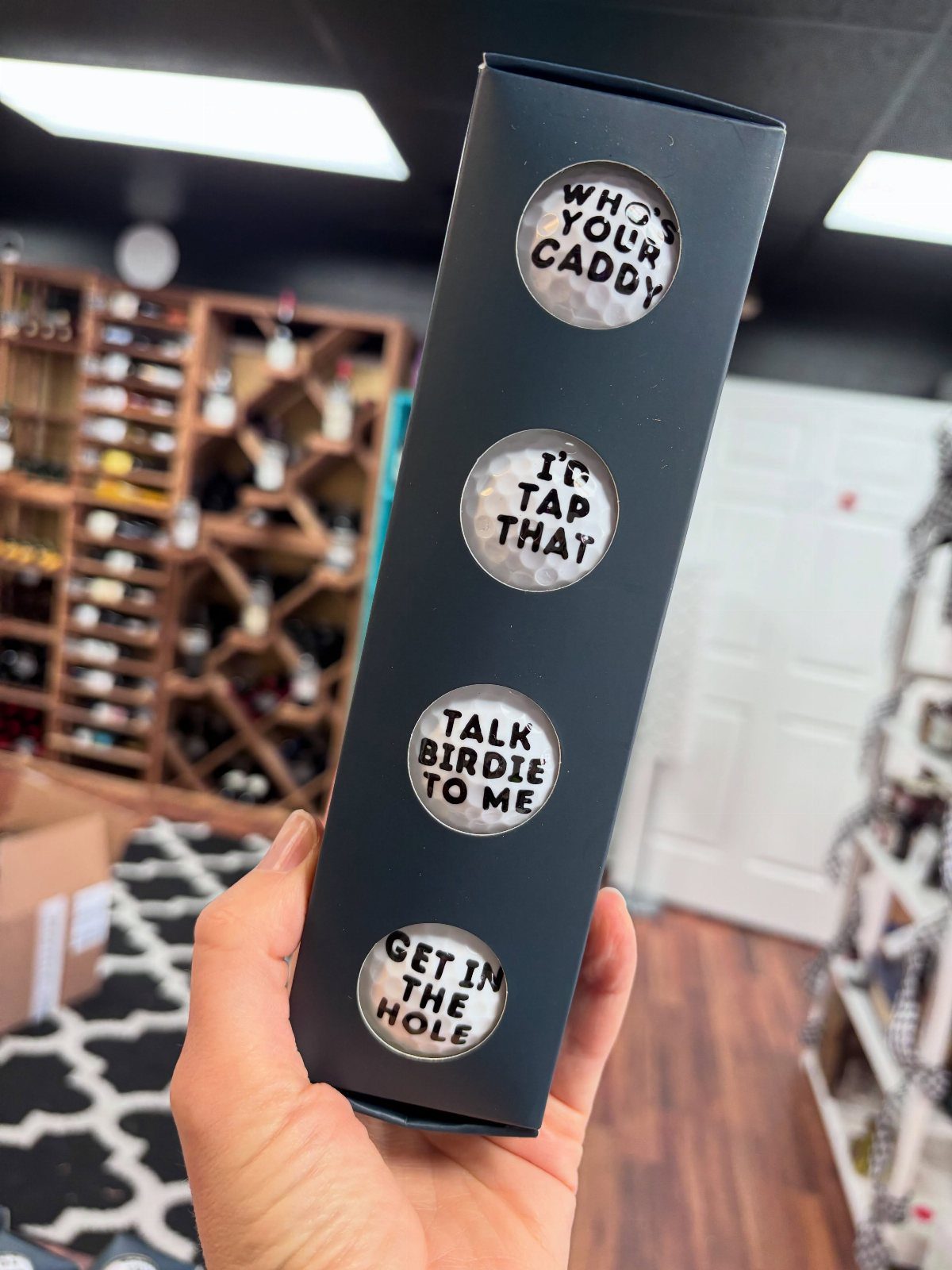 Black box containing four white golf balls with funny golf-themed sayings printed on them.