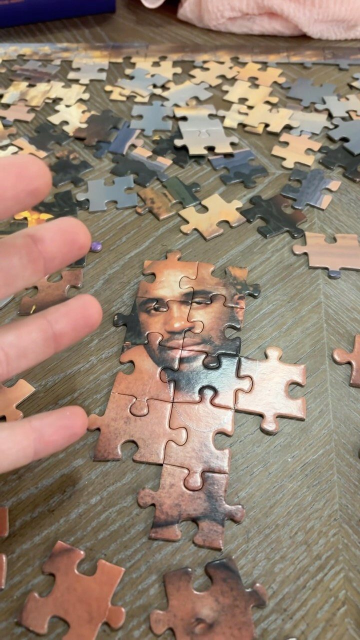 Hand assembling a custom jigsaw puzzle featuring a man's face on a wooden table