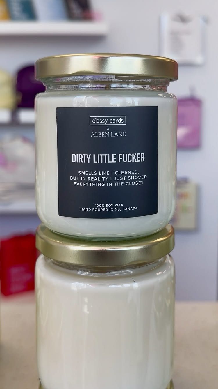 Two white soy candles in glass jars with a humorous black label.