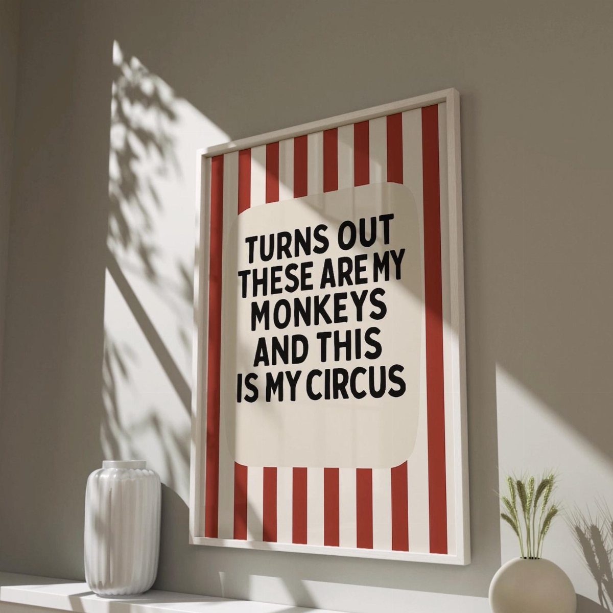 Framed humorous print with circus stripes and text leaning against a white wall.