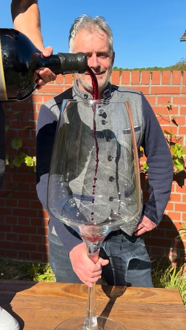 Man pouring red wine into a giant oversized wine glass on a table