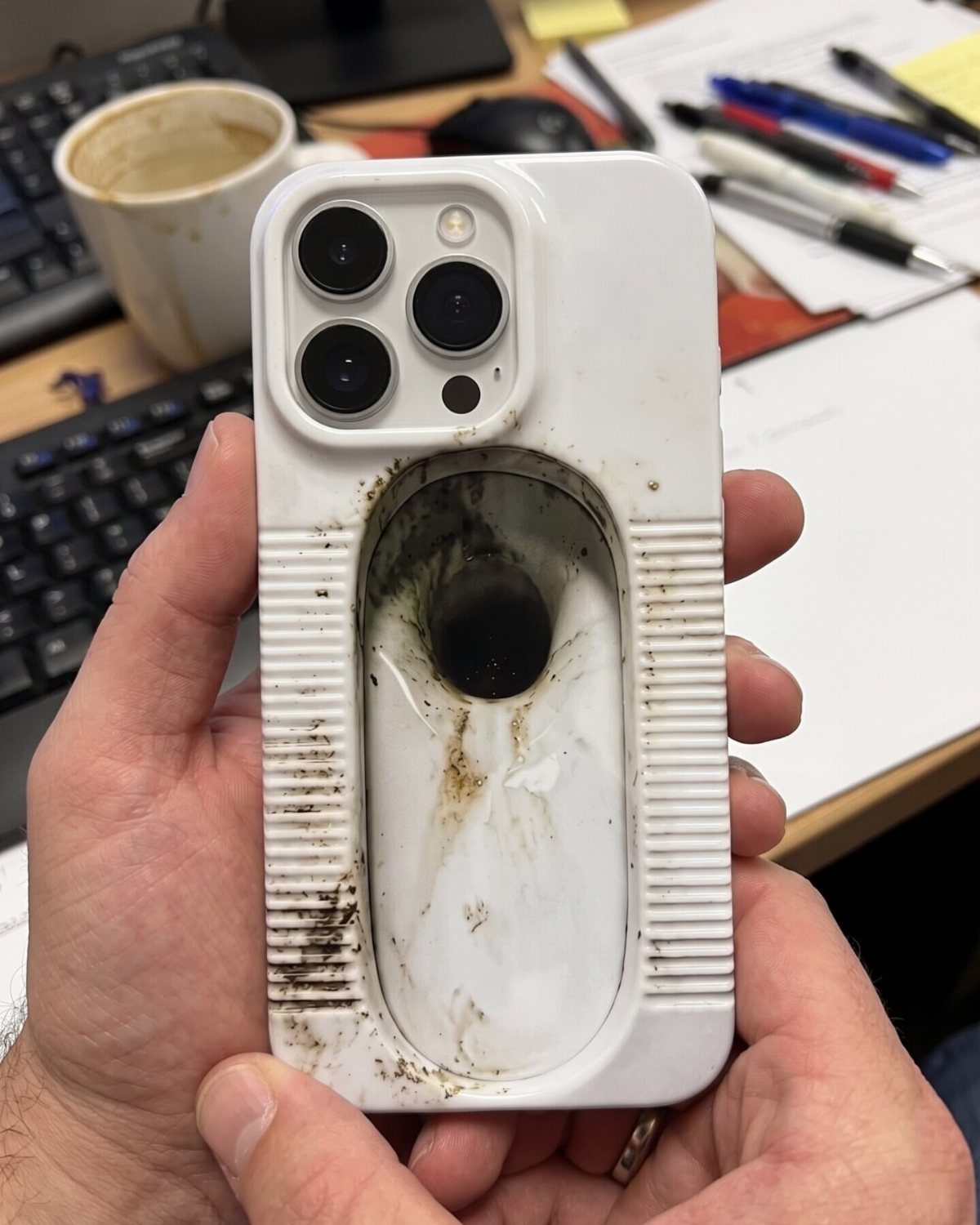 White smartphone case shaped like a dirty toilet held by two hands.
