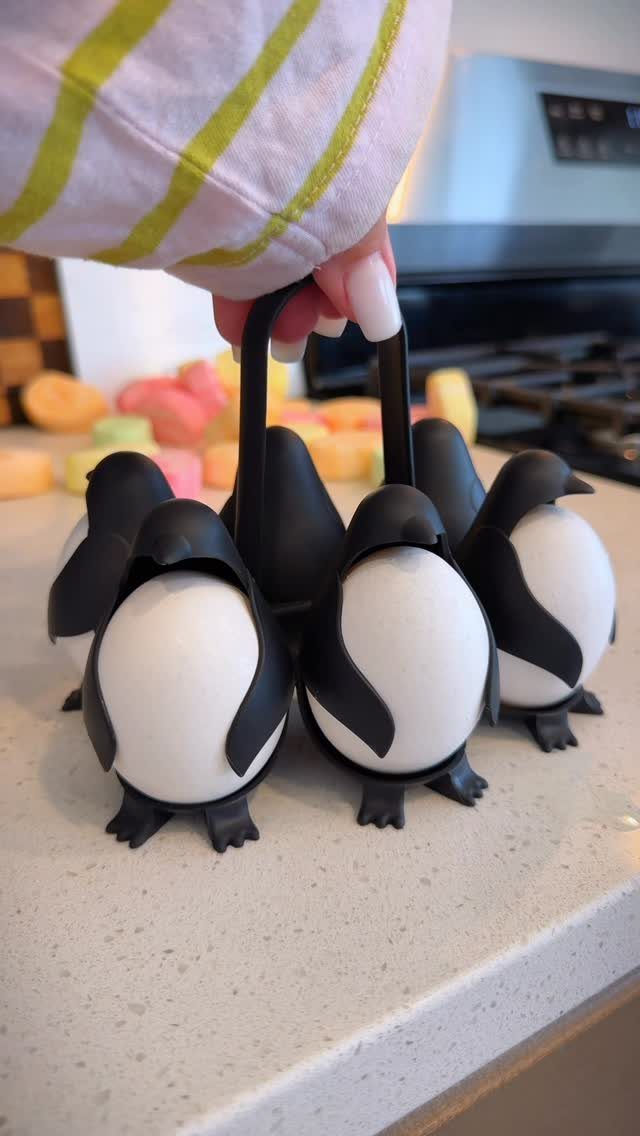 Penguin-shaped egg cups holding white eggs in a black plastic carrier on countertop