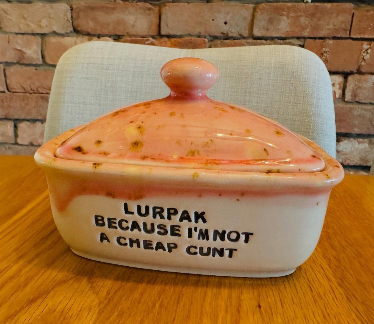 Ceramic butter dish with a pink lid and profane text on the white base.