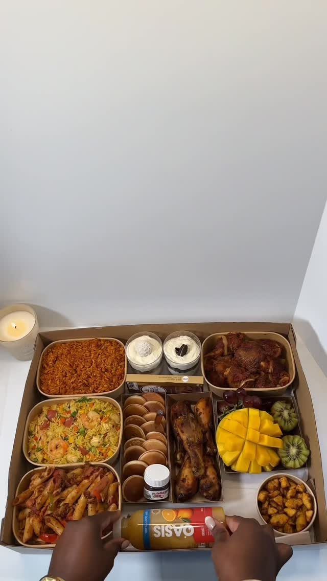 Assorted food platter in a cardboard box with rice, chicken, and fruit.