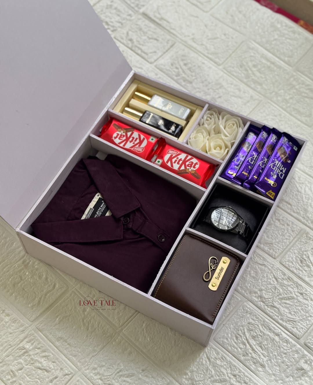 Gift box with maroon shirt, brown wallet, wristwatch, chocolates, and perfume bottles.
