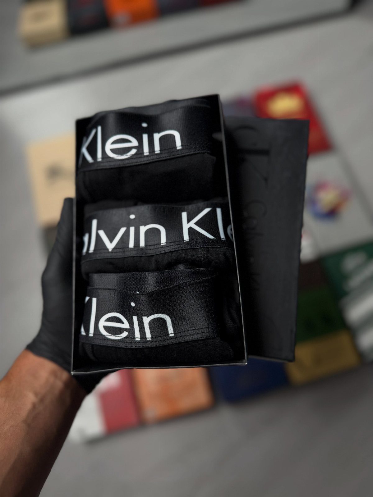 Black Calvin Klein boxers in a black gift box held by a gloved hand.