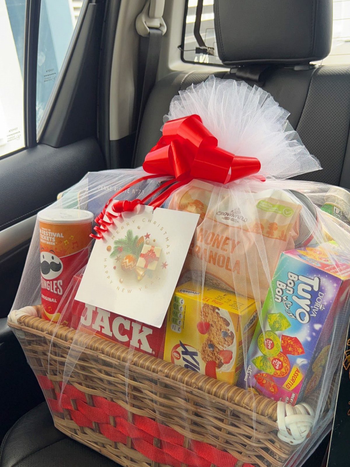 Wicker gift basket filled with snacks wrapped in cellophane with a red bow.