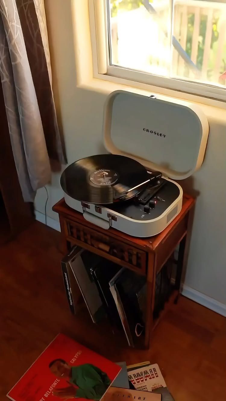 White record player on a wooden table with vinyl records stored underneath.