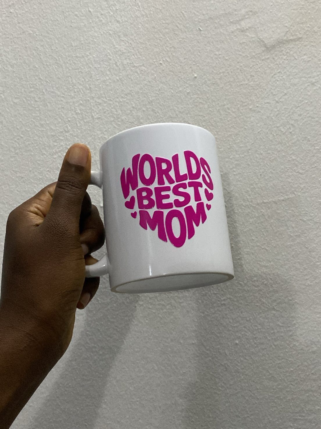 White ceramic mug with pink World's Best Mom text held by a hand.