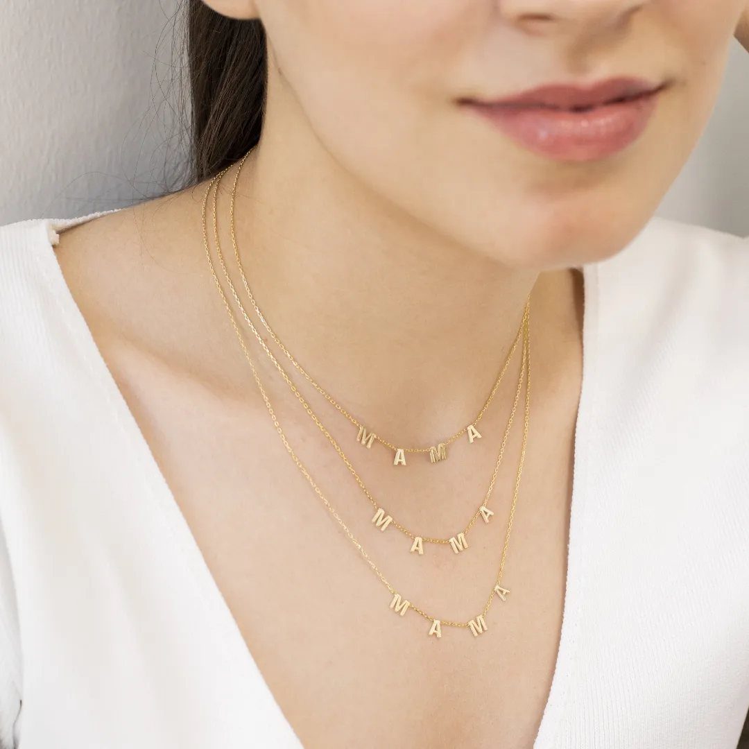 Three layered gold necklaces with MAMA pendants worn by a woman in white.
