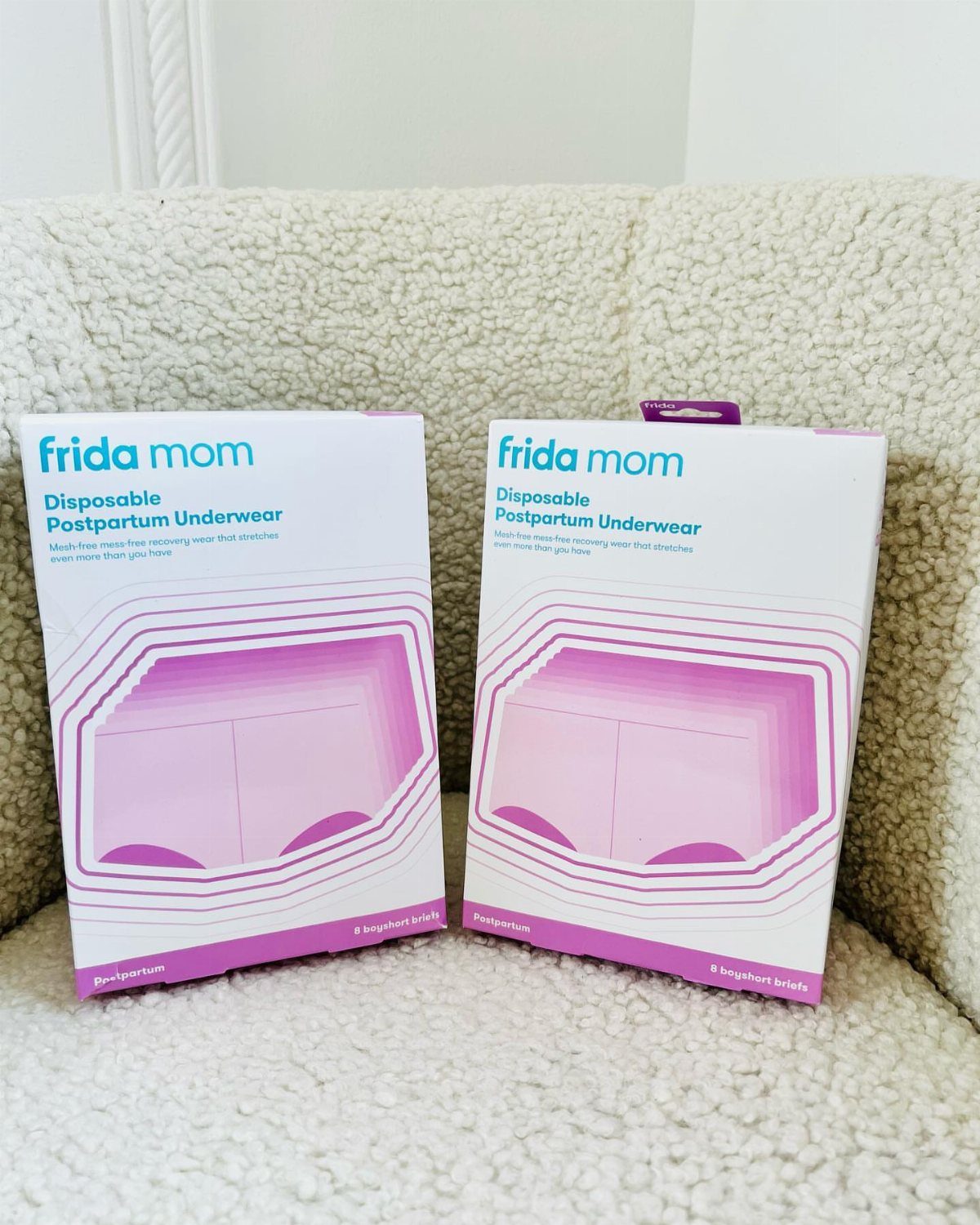 Two boxes of Frida Mom disposable postpartum underwear on a white fuzzy surface.