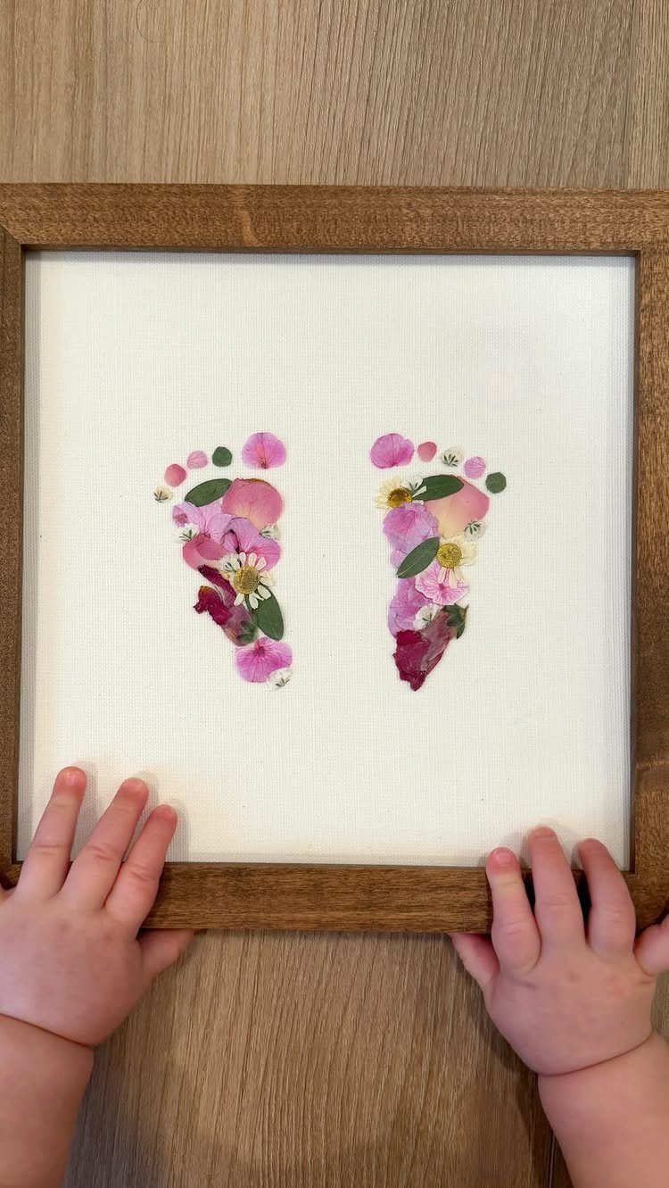 Pressed flower petals forming baby footprints in a wooden frame held by baby hands