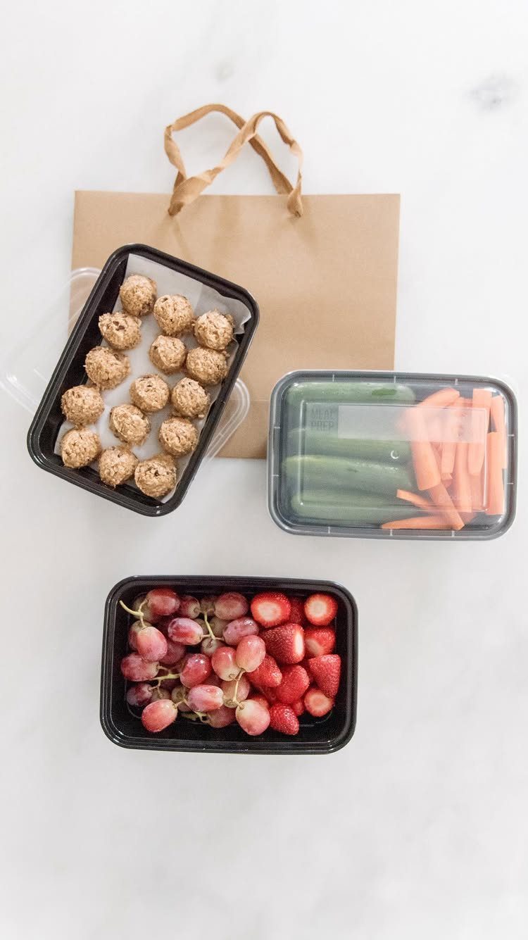 Healthy snacks in containers including fruit, vegetables, and energy balls on marble.