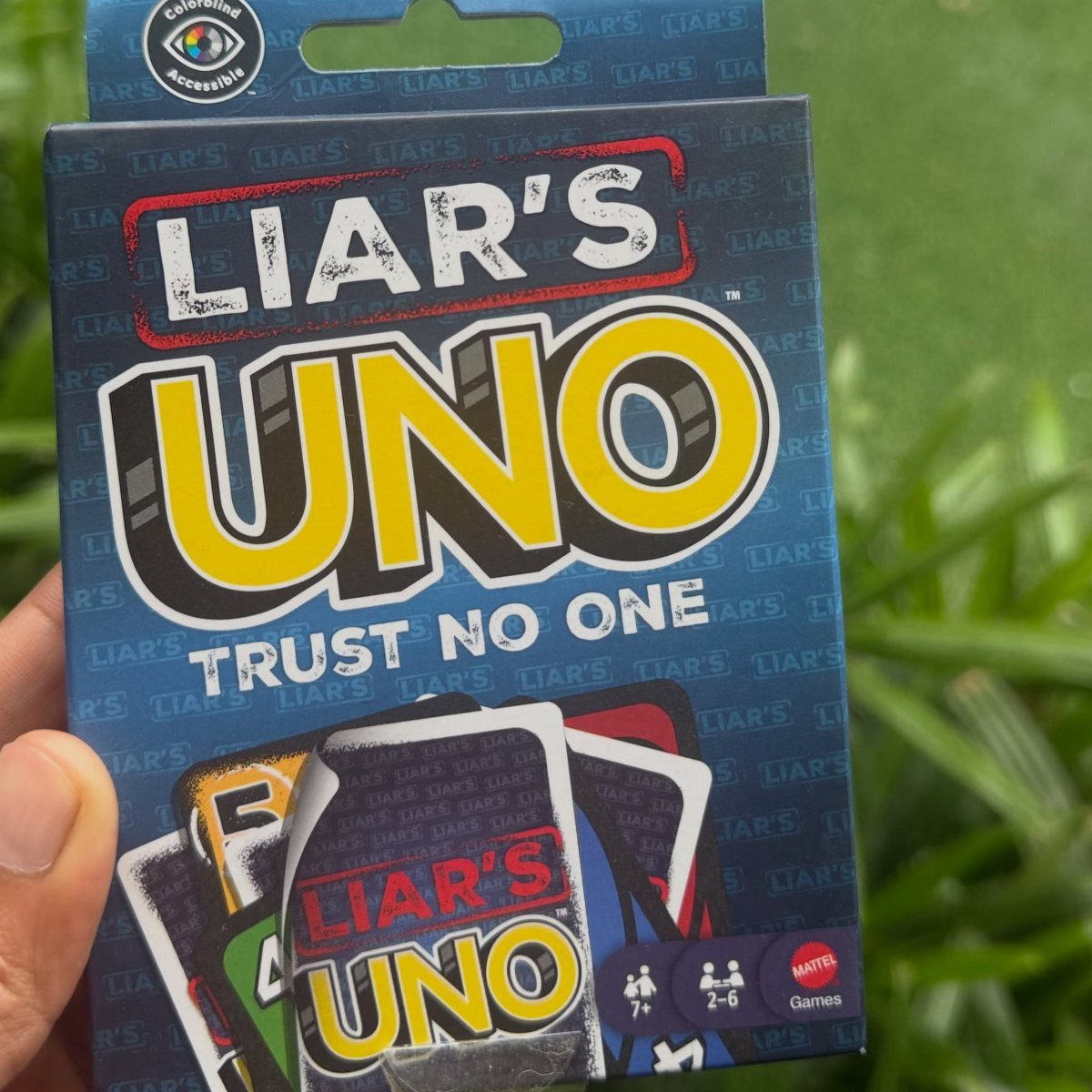Liar's Uno card game box held against a background of green leaves.