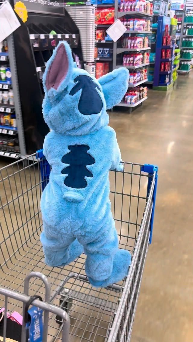 Blue Stitch character costume standing inside a metal shopping cart in a store.