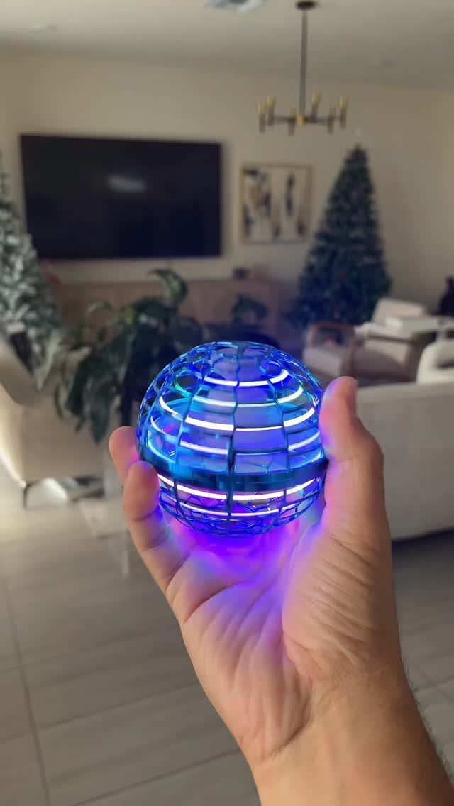 Blue glowing flying orb toy held in a person's hand in a living room.