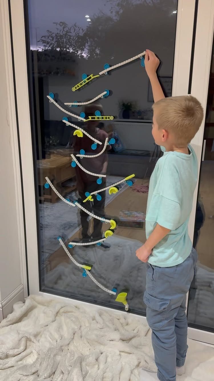 Young boy building a marble run set on a glass sliding door.