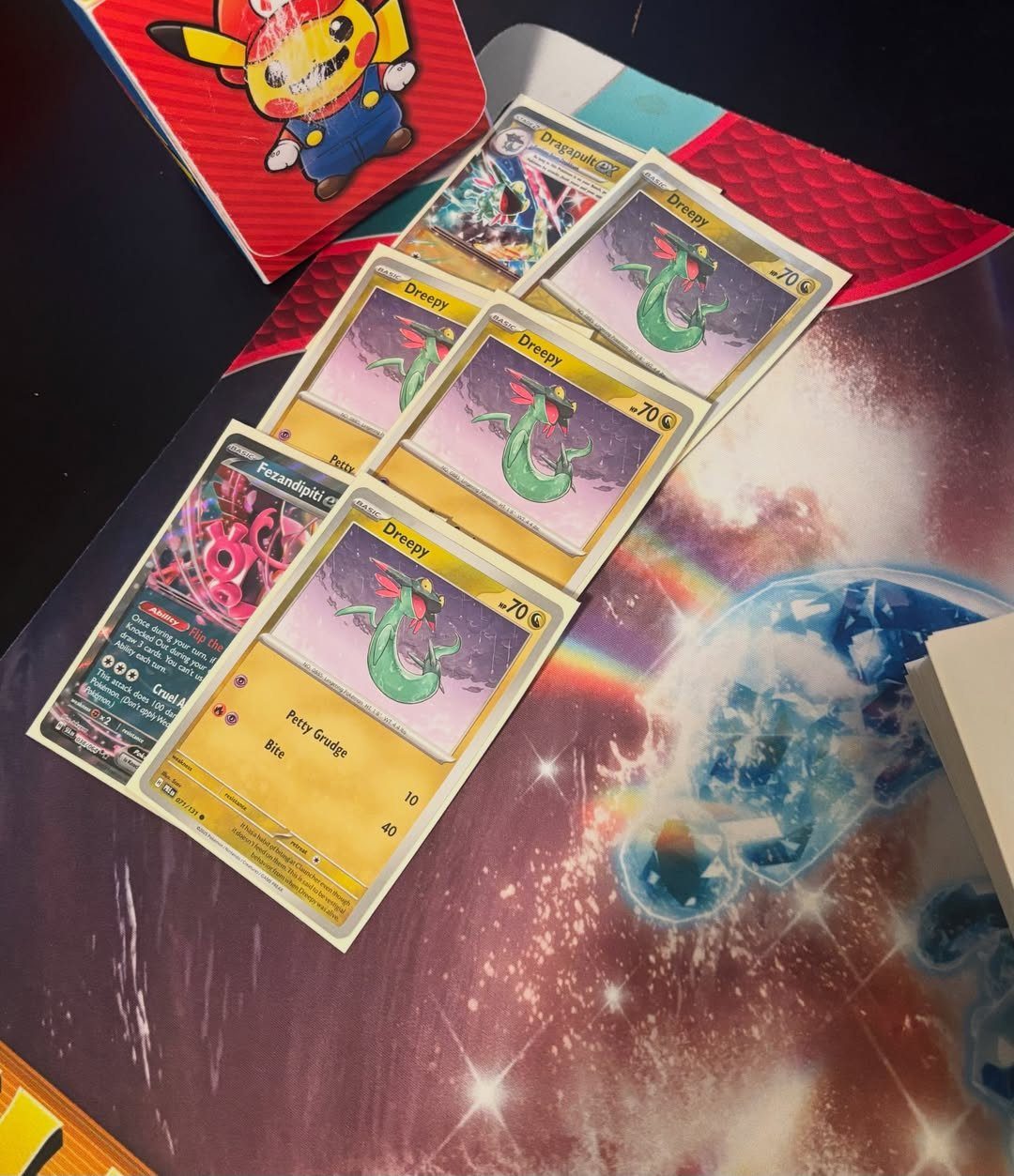 Pokemon trading cards and a Pikachu binder on a cosmic space playmat