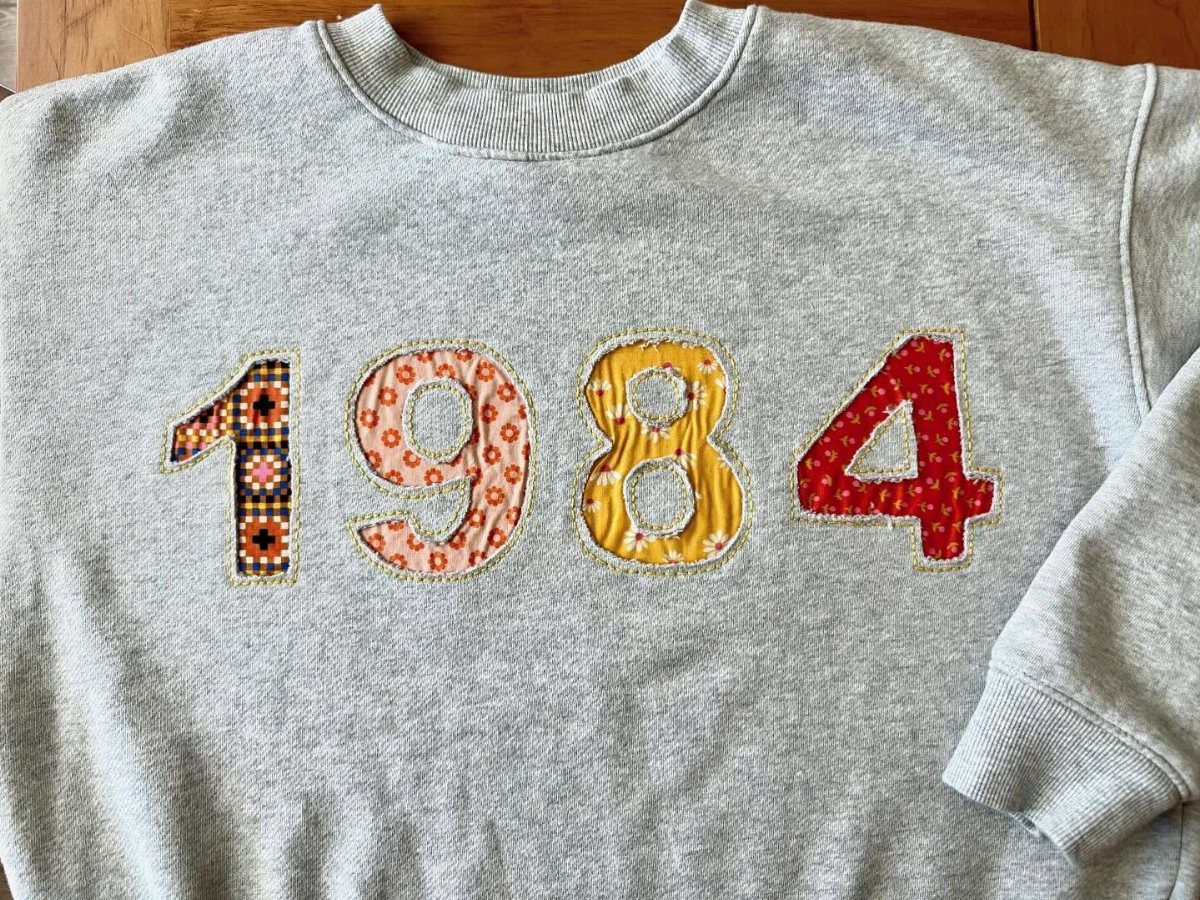 Grey sweatshirt with the year 1984 in colorful patterned fabric patches.