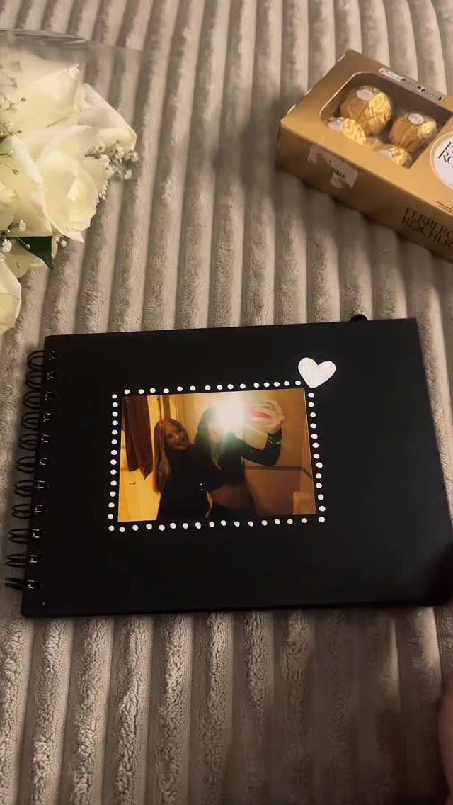 Black scrapbook with a photo and heart sticker, white roses, and chocolates.