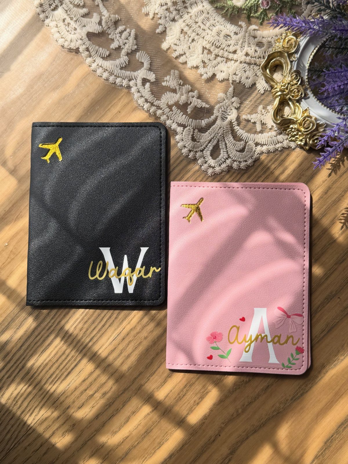 Personalized black and pink passport holders with initials and names on wooden surface