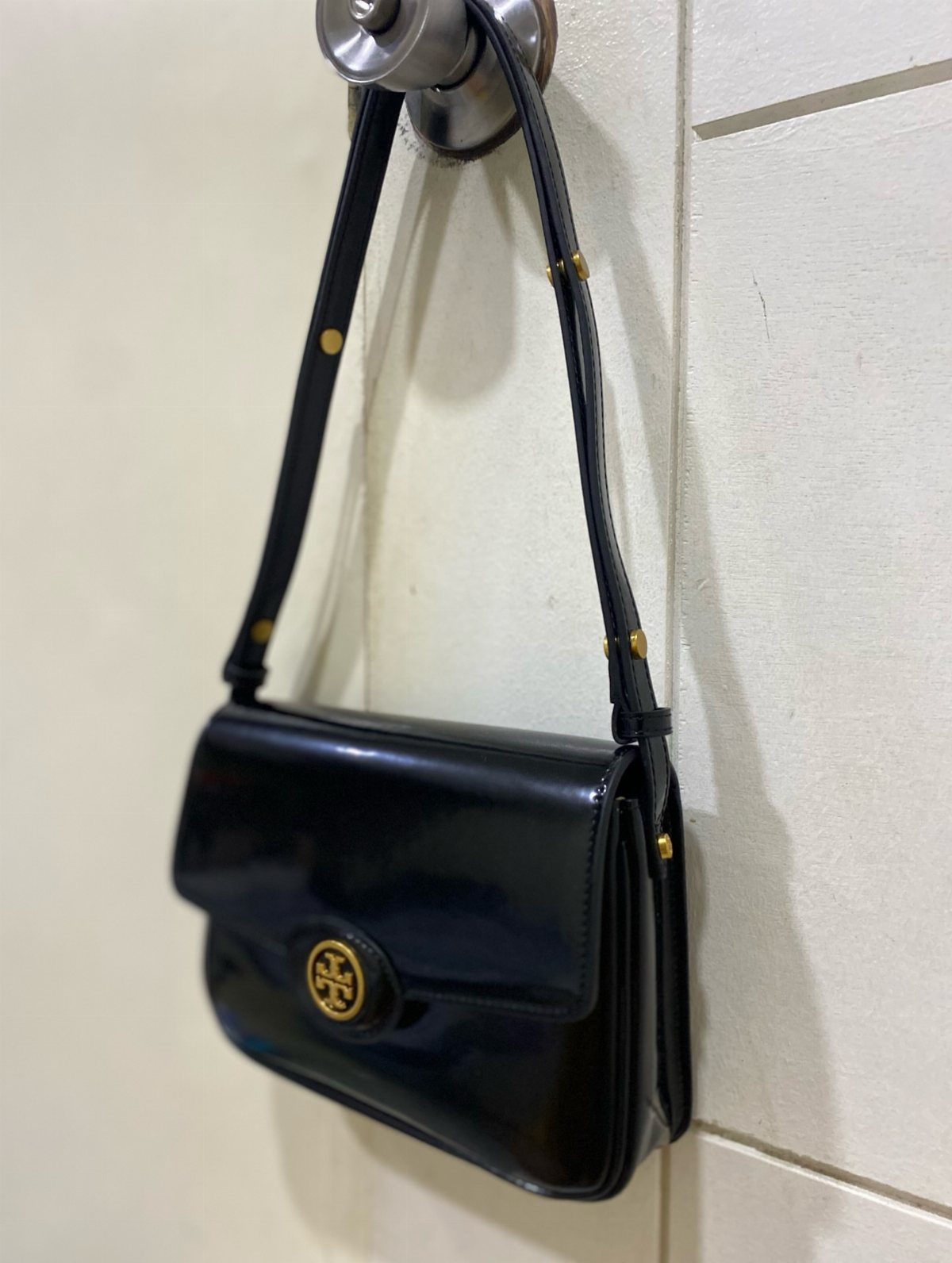 Glossy black leather handbag with gold hardware hanging from a silver door knob