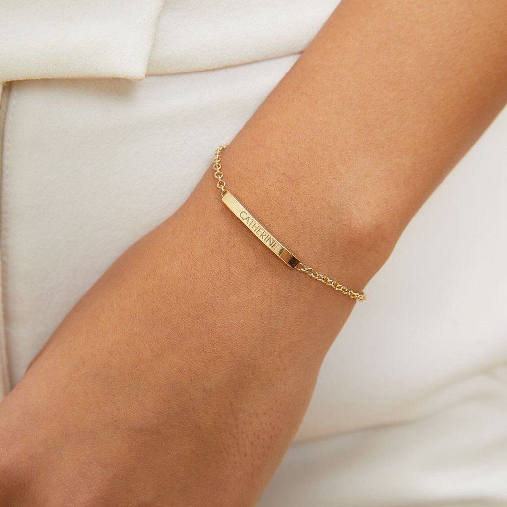 Gold personalized name bracelet on a wrist against a white background
