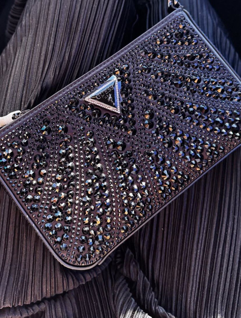 Black rhinestone clutch bag with a silver triangular clasp on pleated purple fabric