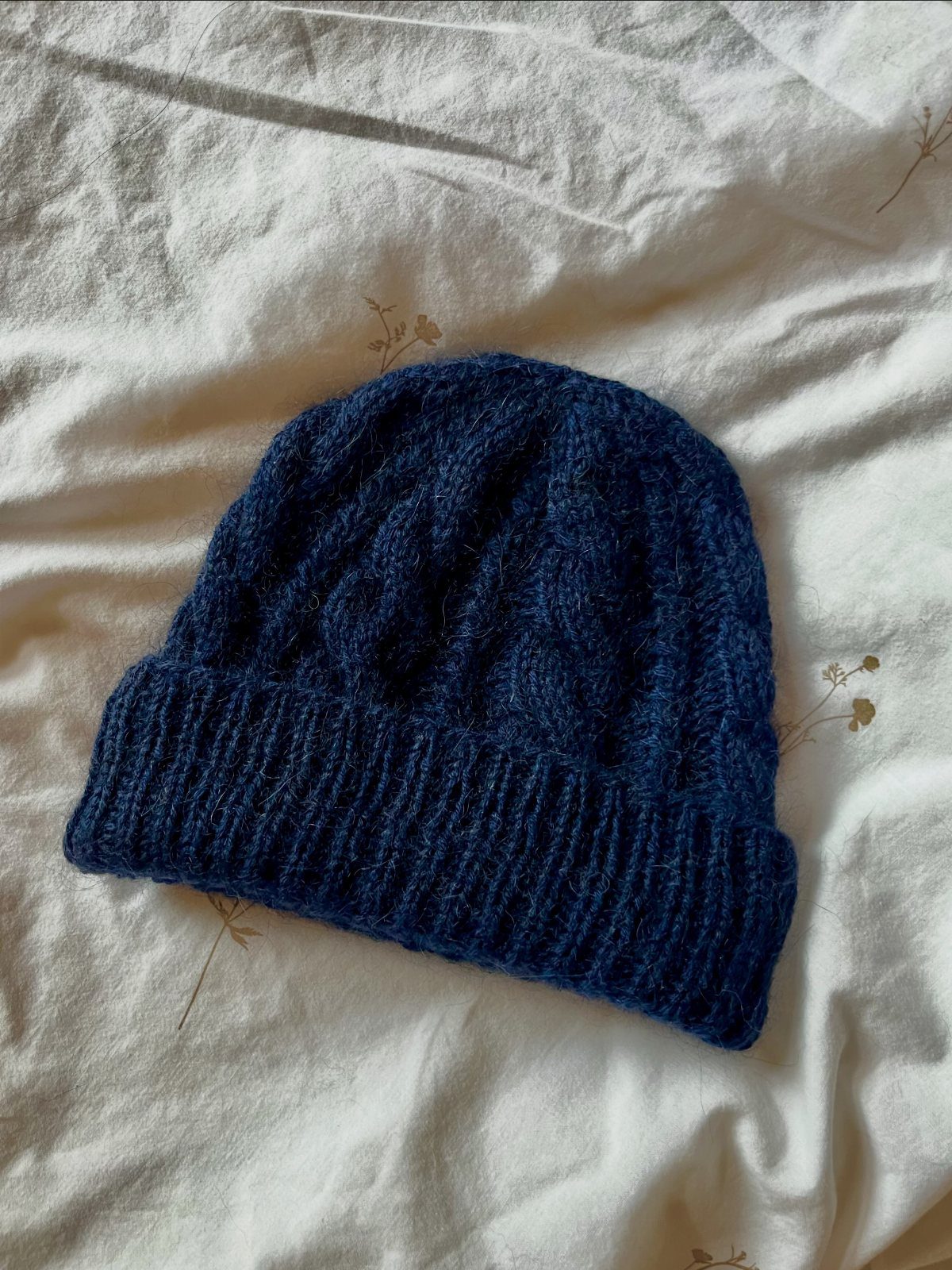 Navy blue chunky cable-knit beanie hat on a white floral fabric background.