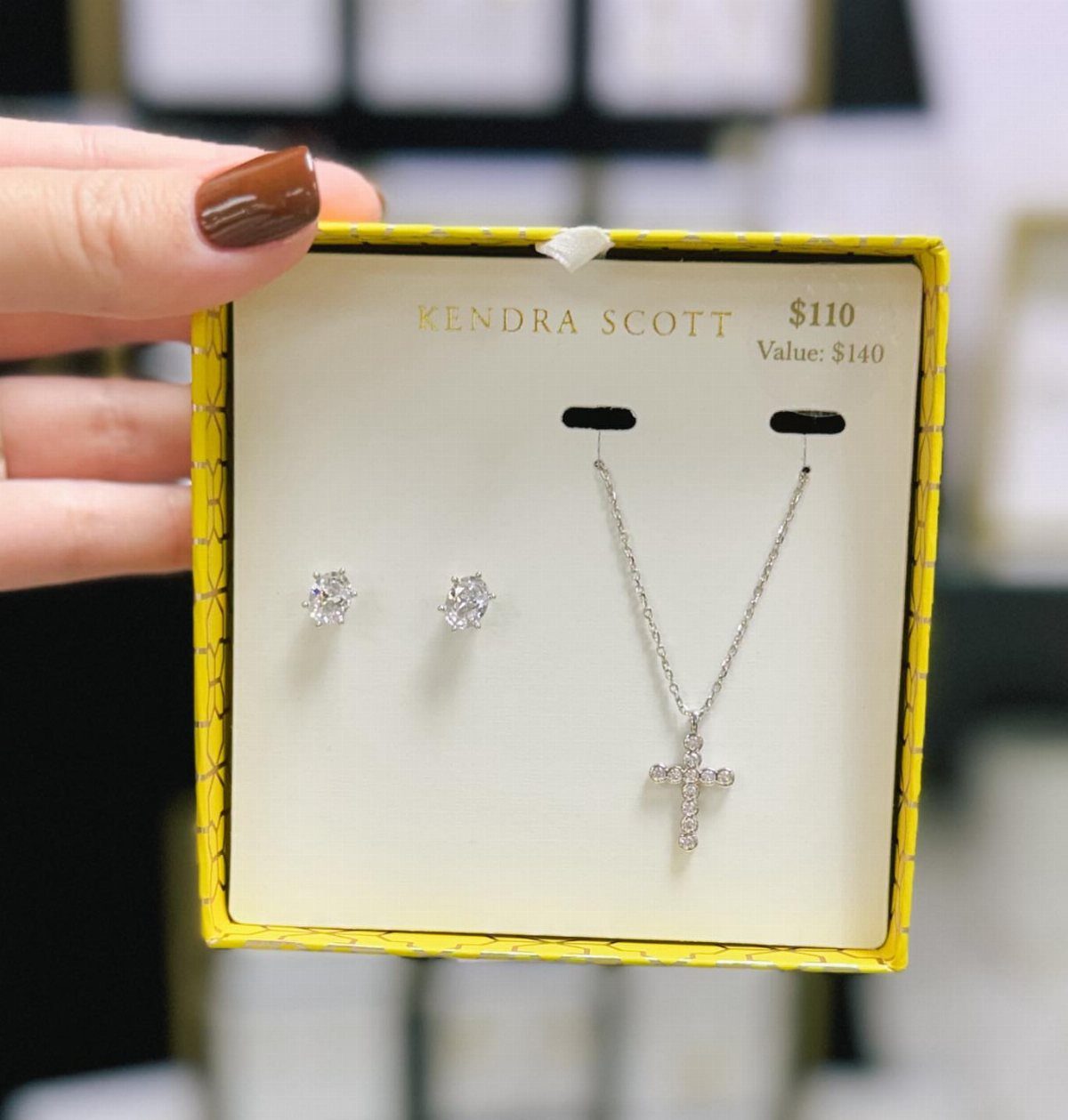 Silver cross necklace and stud earrings in a yellow Kendra Scott jewelry box