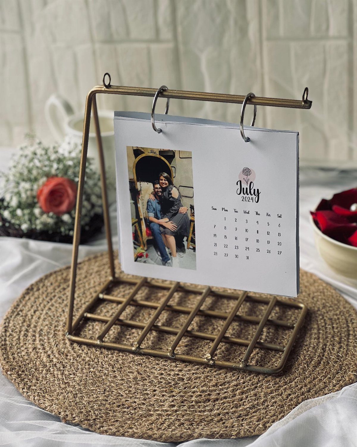 Personalized photo calendar on a brass easel stand resting on a woven mat.