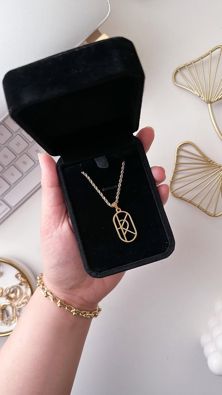 Gold necklace with geometric pendant in a black velvet box held by hand