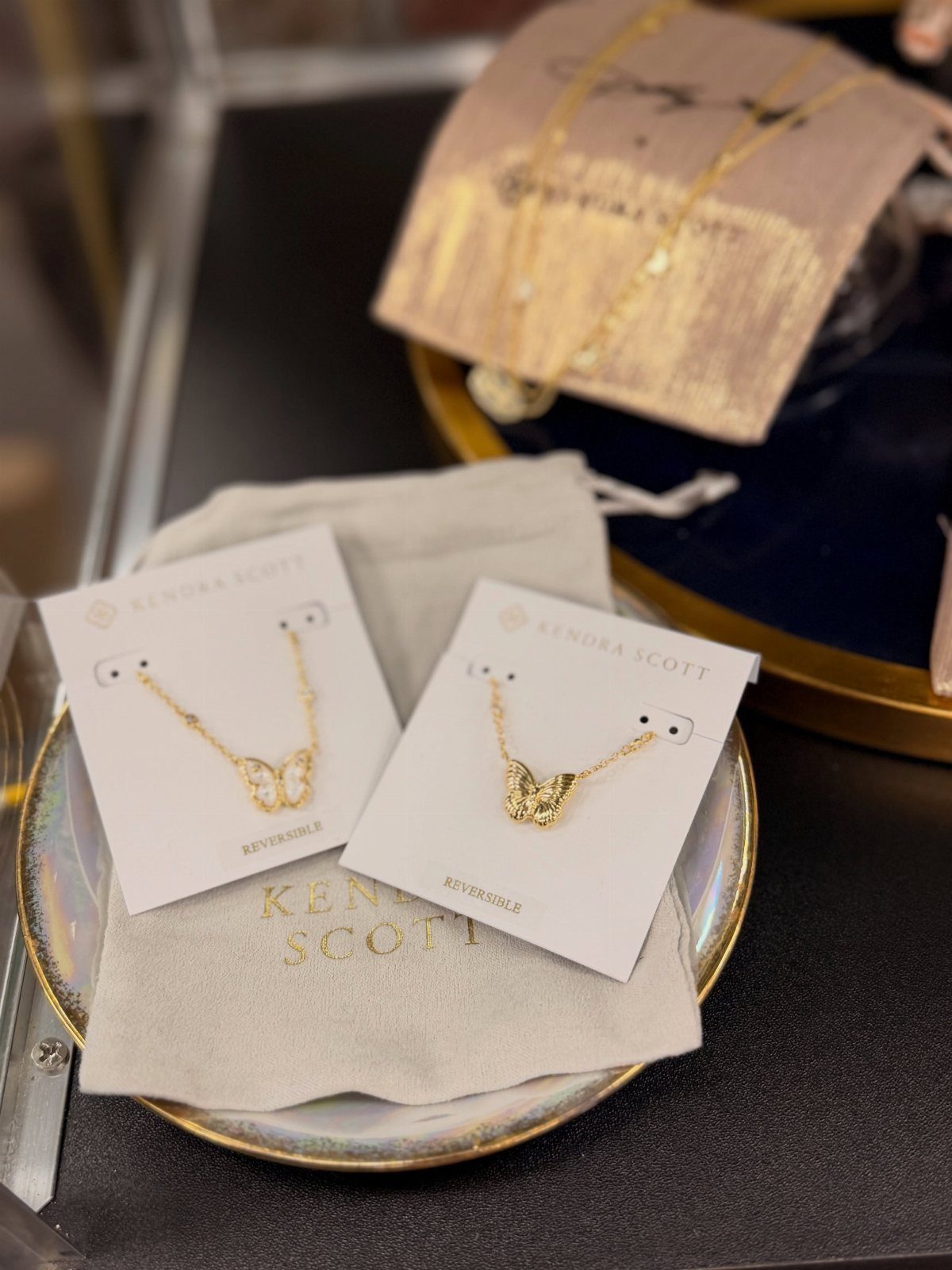 Two gold butterfly pendant necklaces on branded cards resting on a small dish.