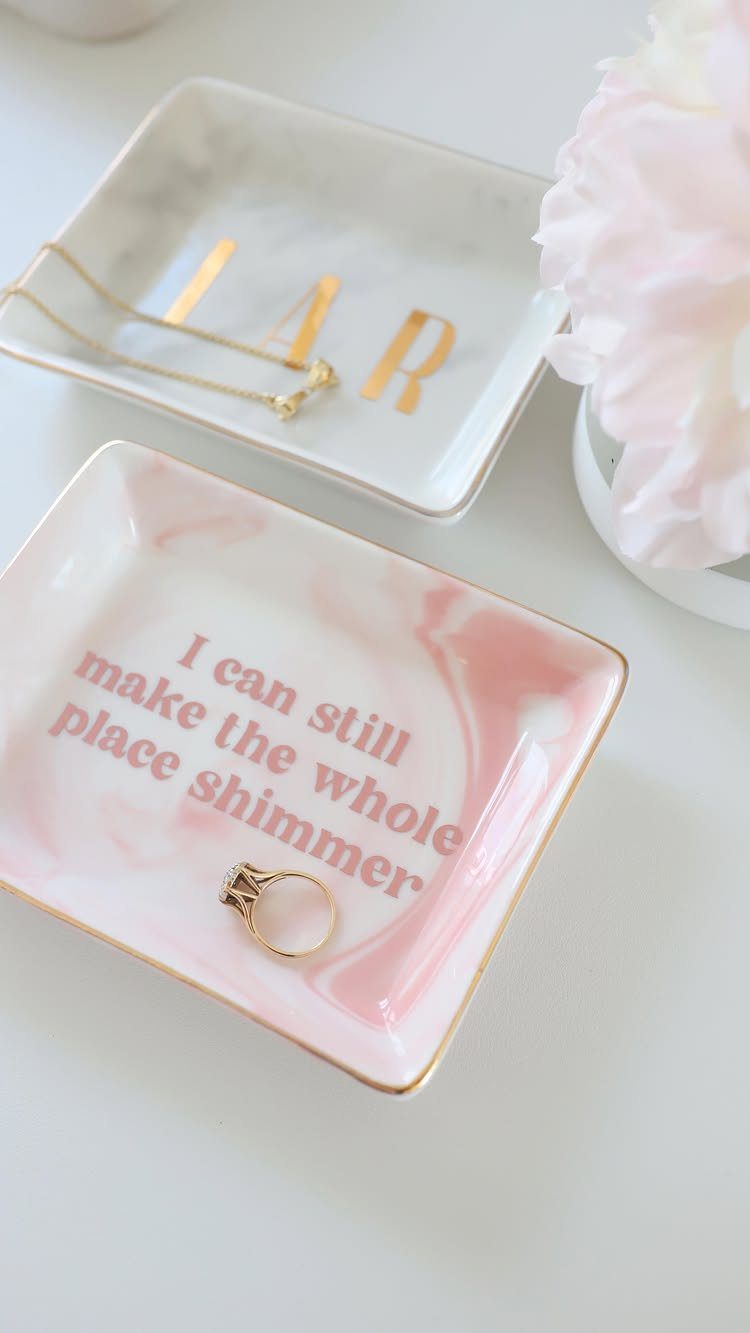 Two ceramic jewelry trays, one with initials and one with a quote, holding jewelry.