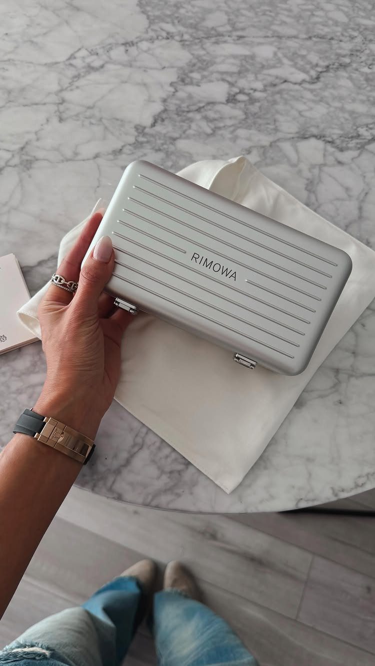 Silver ribbed Rimowa aluminum case held by a hand over a marble table.