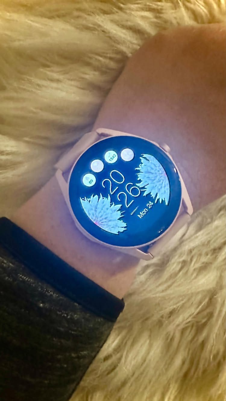 Light pink smartwatch on a wrist resting on white fluffy faux-fur fabric
