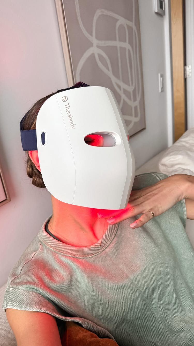 Person wearing a white Therabody LED face mask emitting a red light treatment.