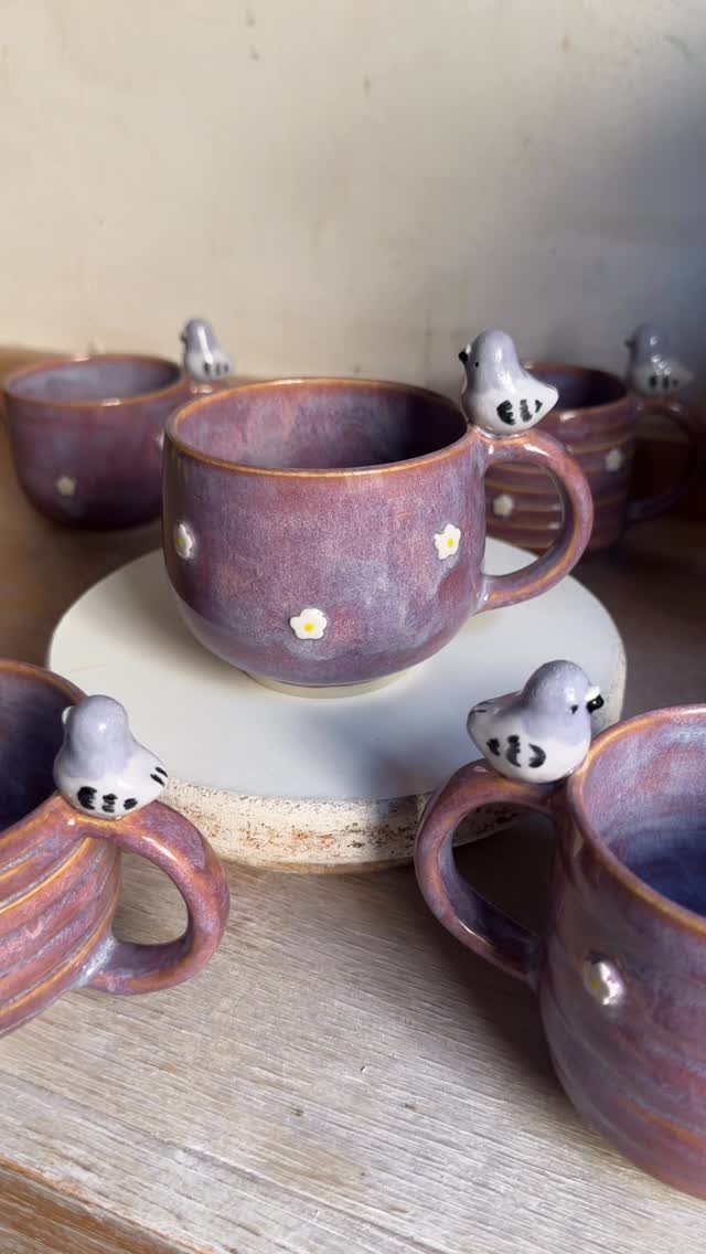 Purple ceramic mugs with small grey birds perched on the handles.