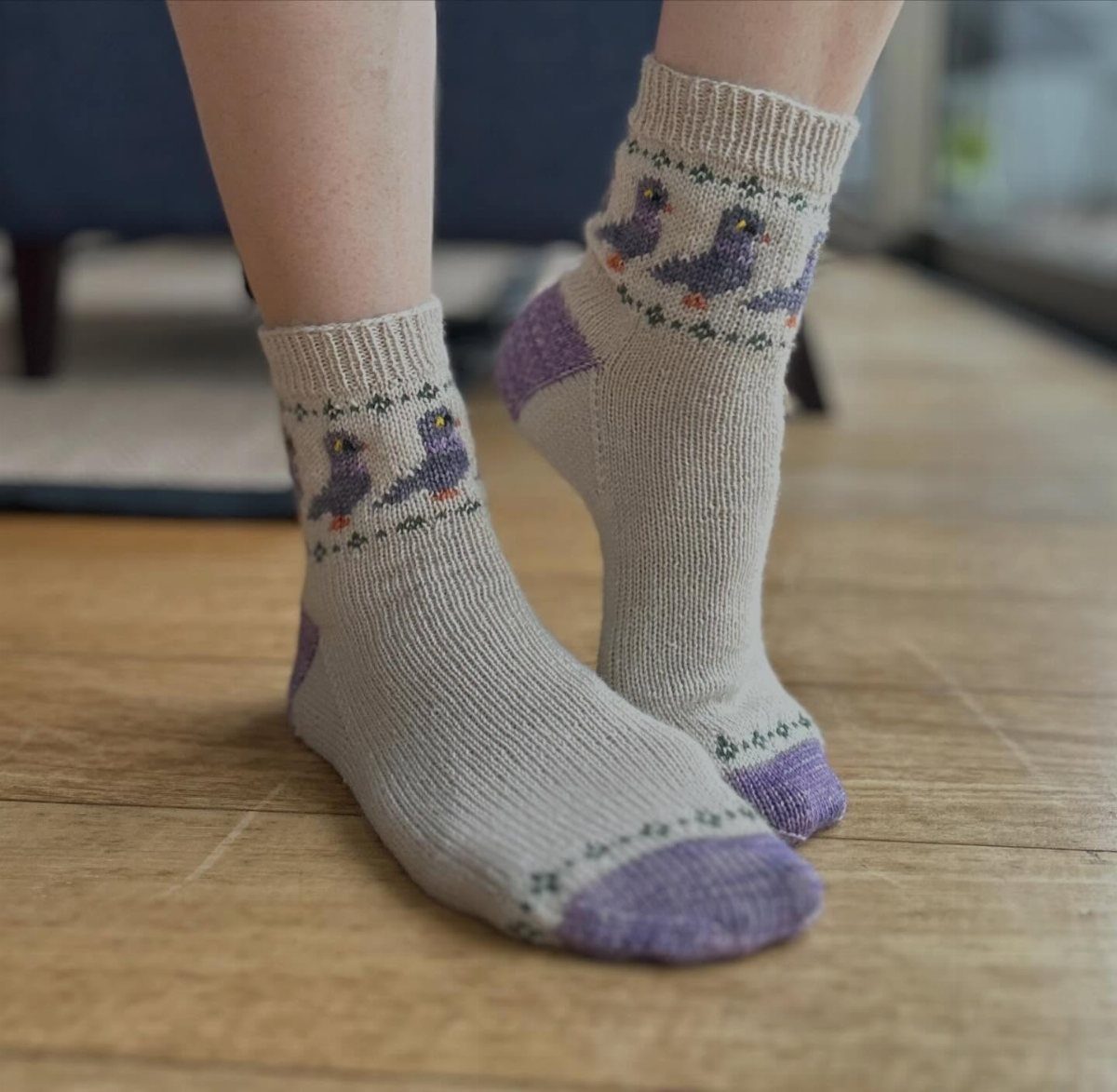 Beige knit socks with purple bird patterns worn on a wooden floor.