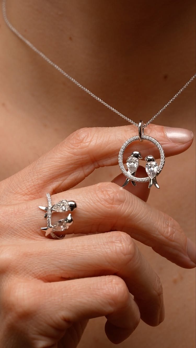 Silver bird pendant necklace and matching ring worn on a person's hand and neck