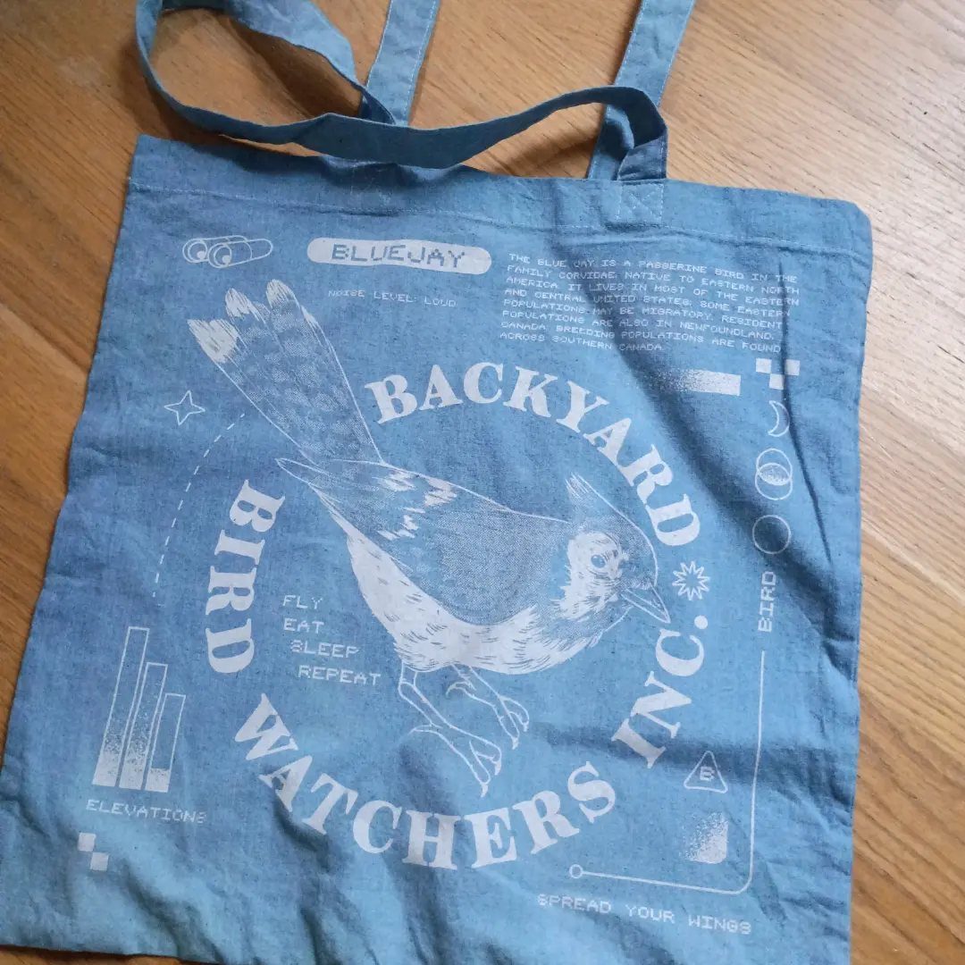 Blue fabric tote bag with a white blue jay bird and birdwatching text.