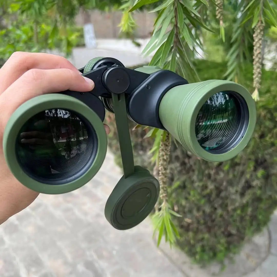 Olive green compact binoculars held by a hand against a leafy green background.