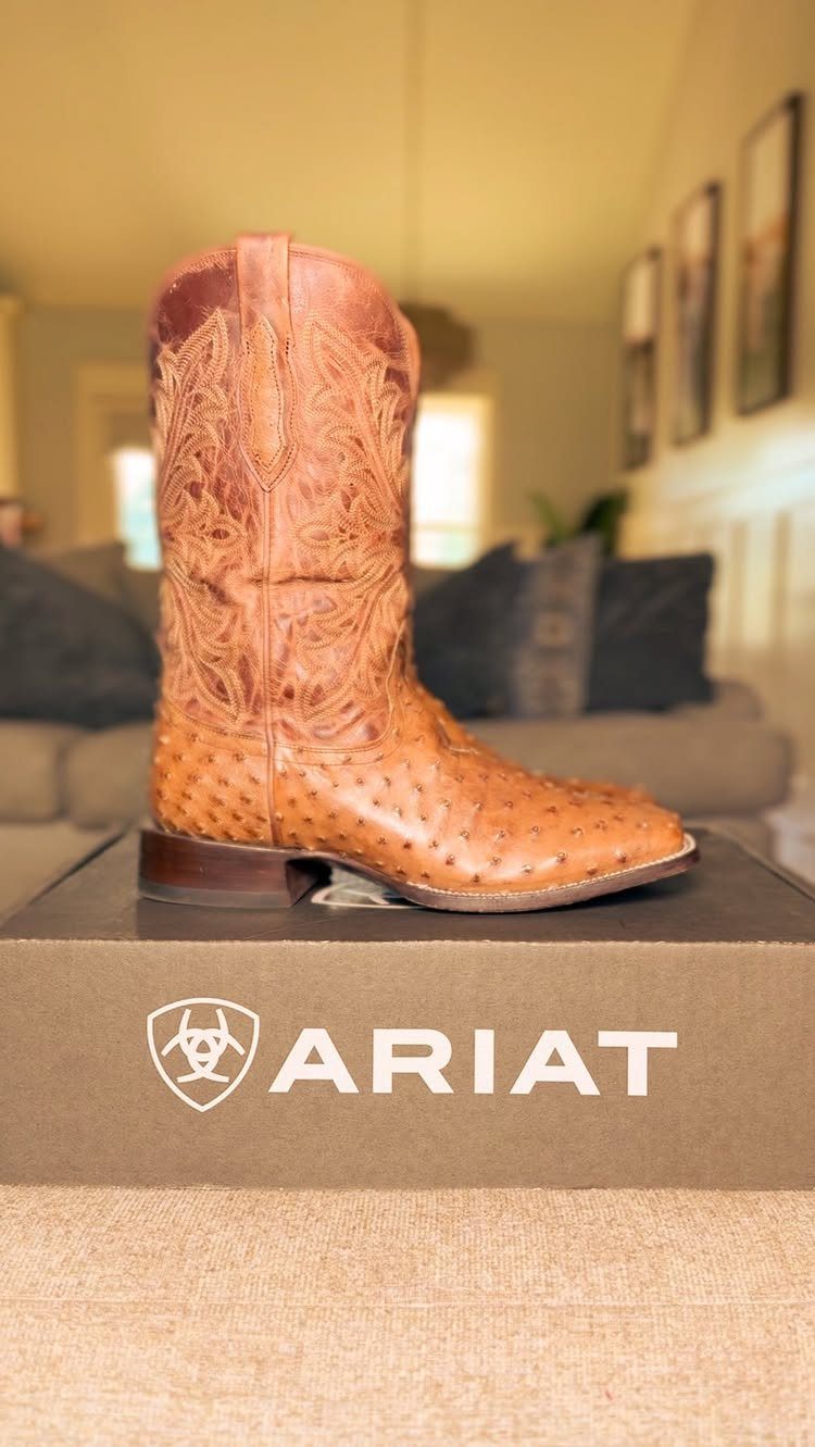 Brown Ariat cowboy boot with ostrich leather resting on its branded shoebox.