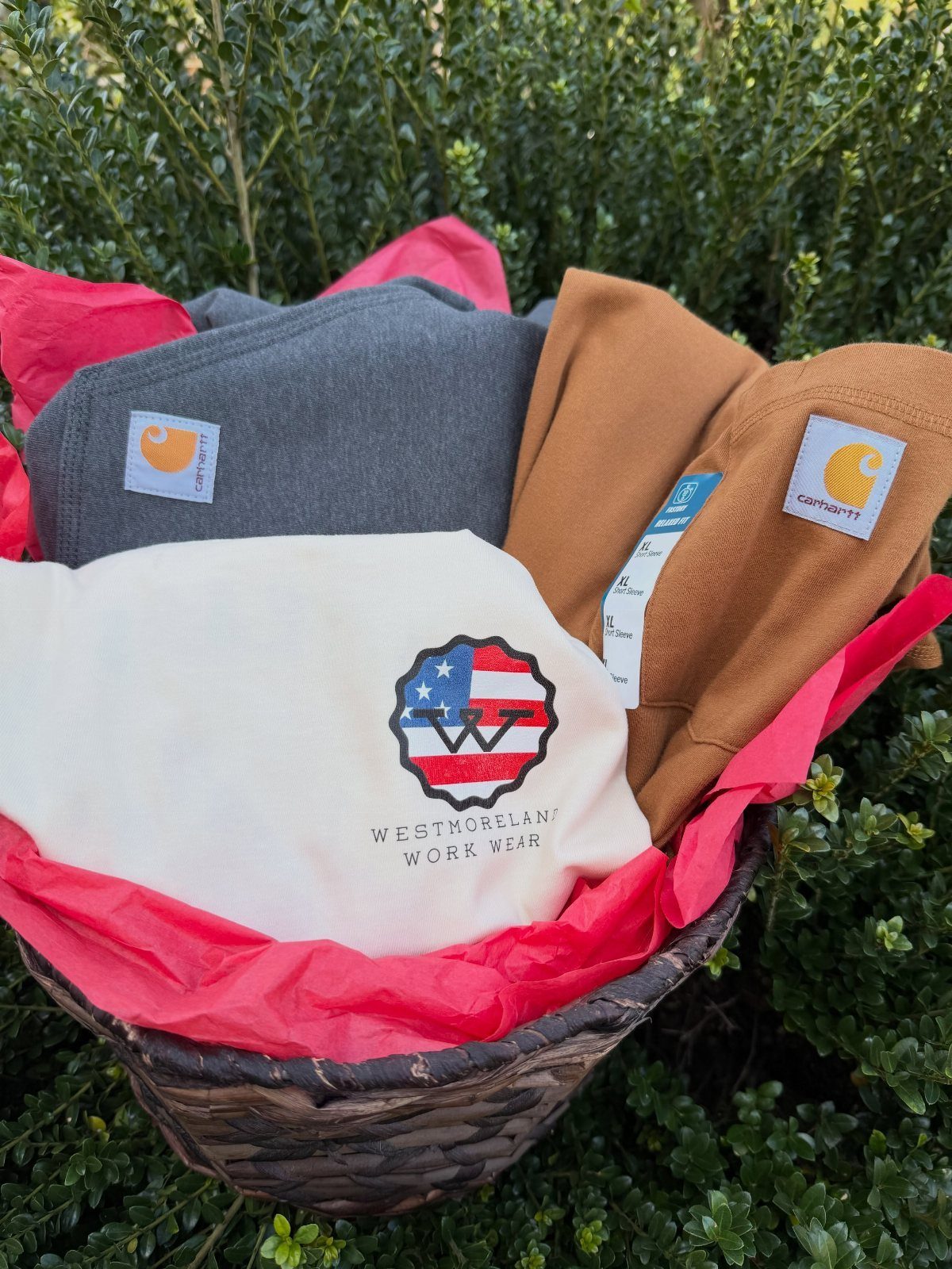 Carhartt workwear clothing folded in a gift basket with red tissue paper.