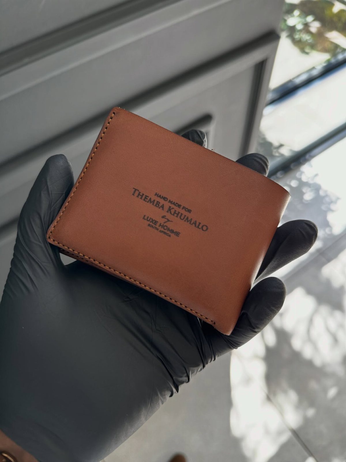 Brown leather personalized wallet held by a hand in a black glove