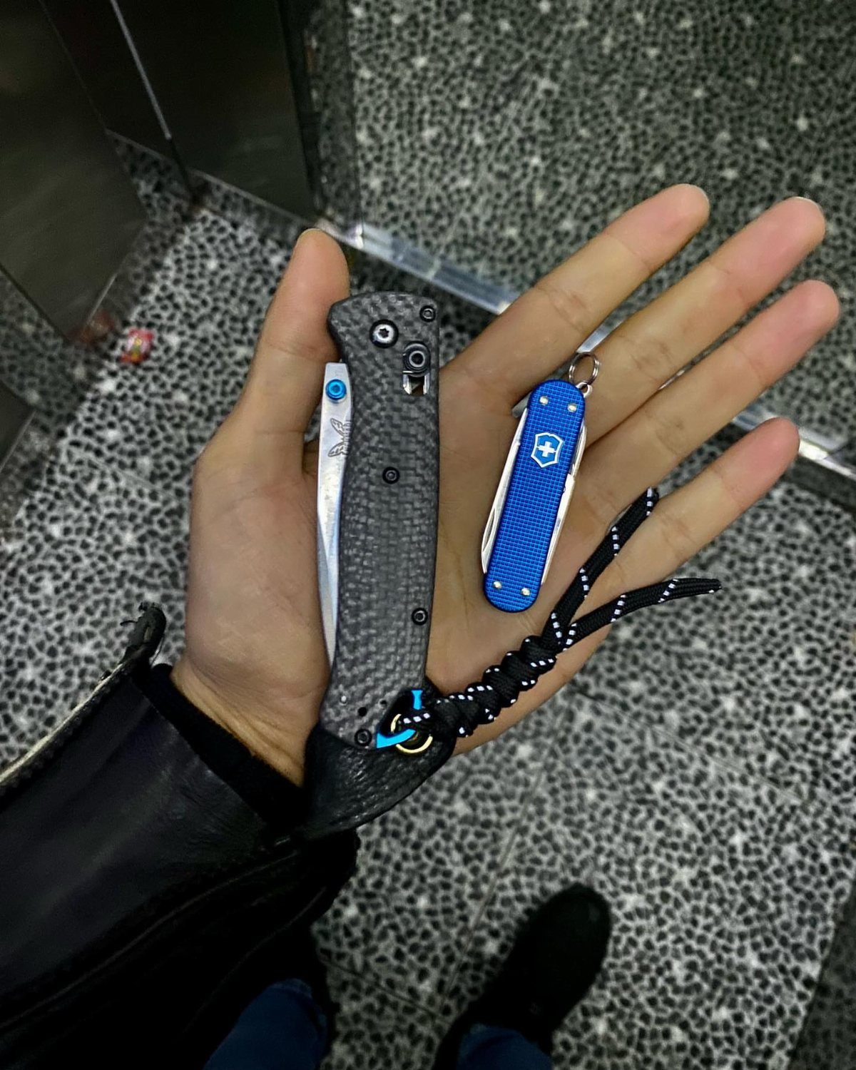 Two pocket knives, one black and one blue, held in a person's hand.