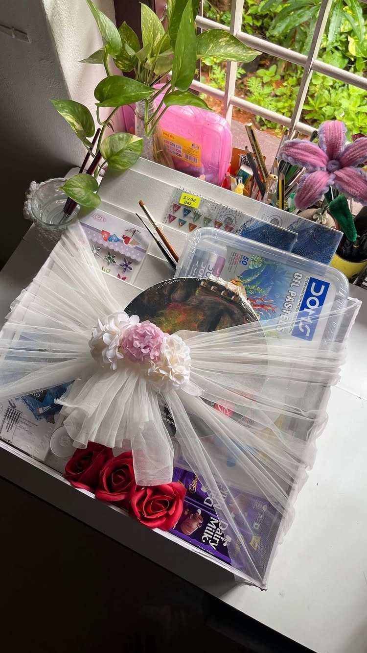 Art supply gift box with oil pastels, decorated with a white tulle bow.