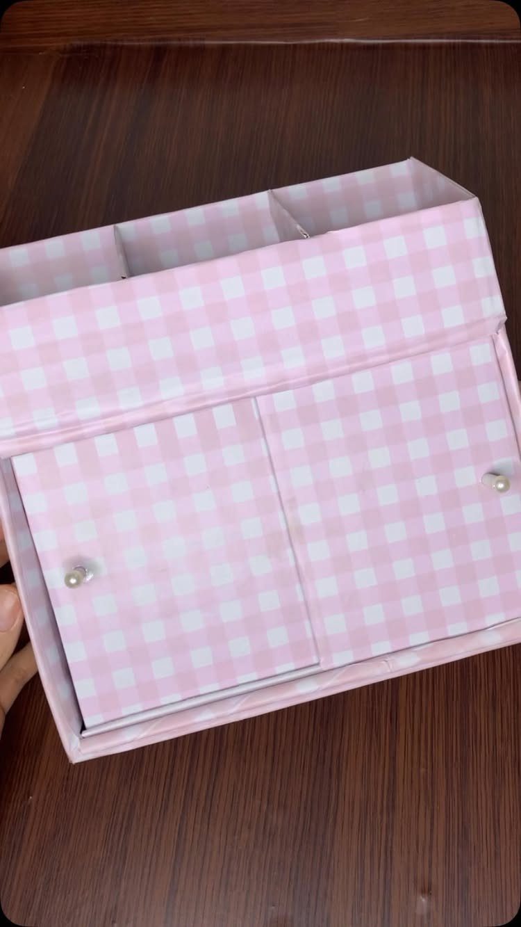 Pink and white gingham storage organizer with drawers on a dark wooden table.