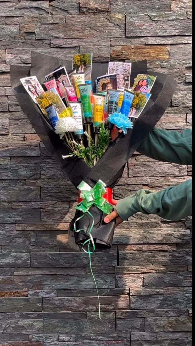 Bouquet of art supplies and photographs wrapped in black paper against stone wall.
